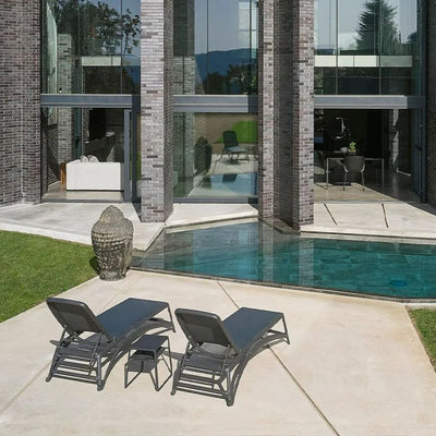 Two black resin 'Nardi' sun loungers with textilene seat and backrest, positioned poolside with one coffee table in between, all facing a super modern house in the outdoor area.