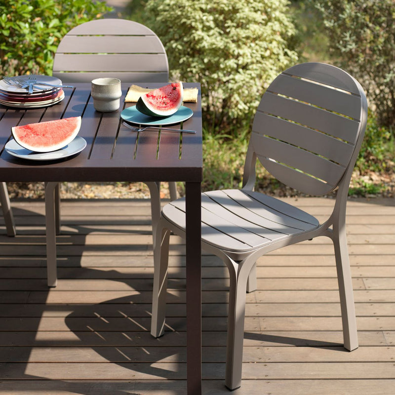 Close-up of outdoor dining chair on sunny patio, part of stylish outdoor setting with plants.