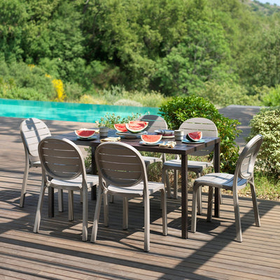 Sunny outdoor setting with outdoor dining table, and outdoor chairs, surrounded by plants.