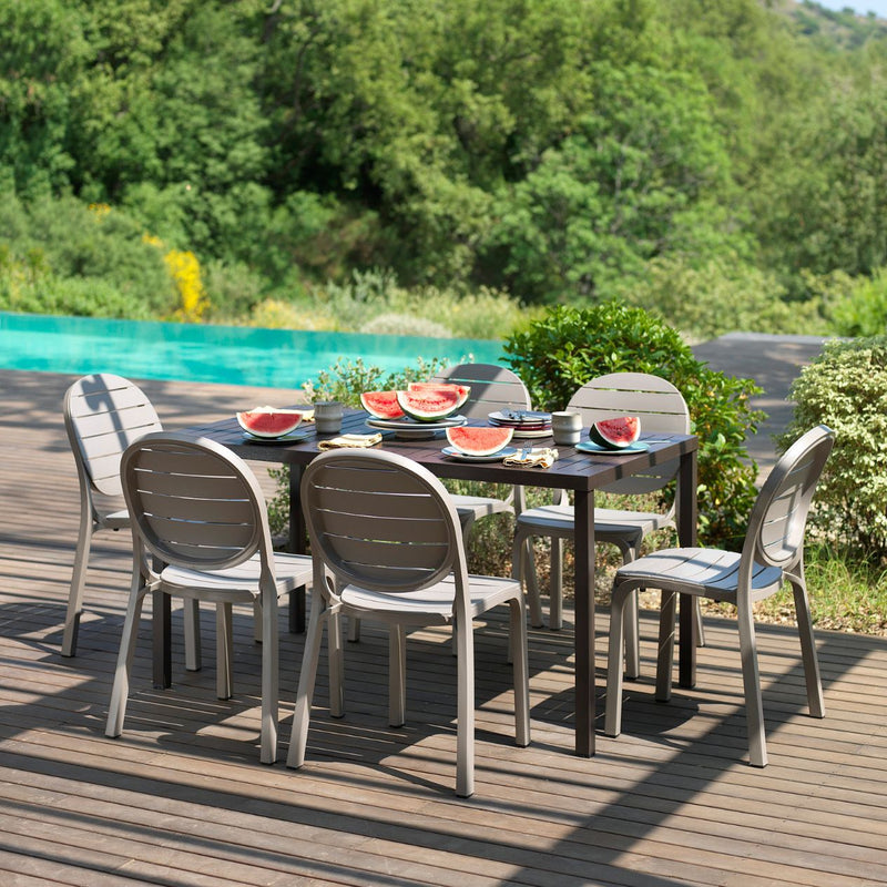 Sunny outdoor setting with outdoor dining table, and outdoor chairs, surrounded by plants.