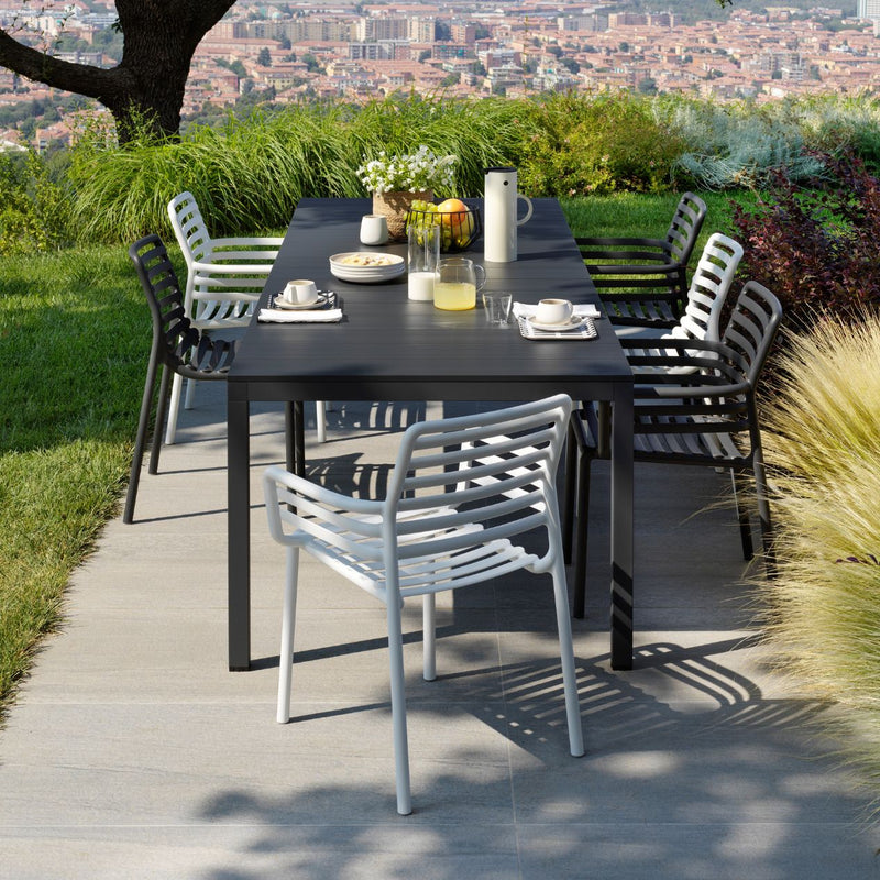 Alfresco furniture setup with black Nardi Rio extension dining table, white and black resin chairs, styled with fruit and drinks, surrounded by greenery with a view of an Italian city in the background.