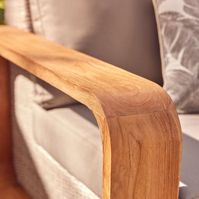 Closeup of a white wicker outdoor lounge with cushioned seat and back, showcasing the teak arm frame.