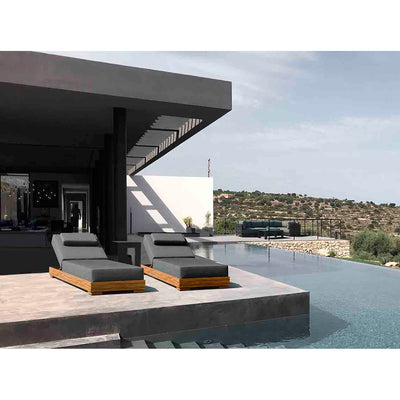 Two grey and brown aluminium 'Skyline' outdoor sun loungers with headrests slightly elevated, set poolside in the outdoor area of a modern house with hills in the background.