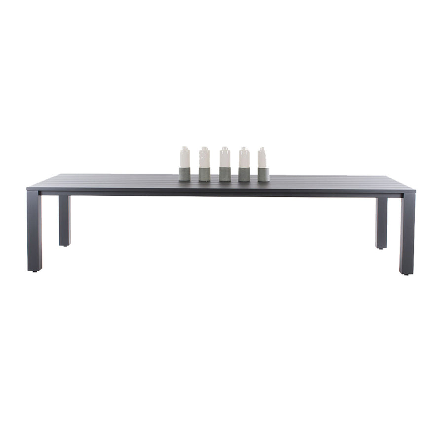 A modern rectangular aluminium outdoor dining table with a sleek black surface and minimalist design, set against a plain white background. The table has 4 white candles on top of it.