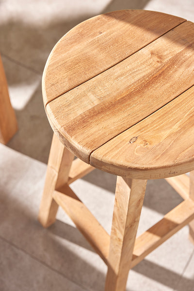 Top-down view of a round teak stool in an outdoor setting, highlighting the rich grain of the teak wood, bathed in sunlight, emphasizing the beauty of teak wood furniture.