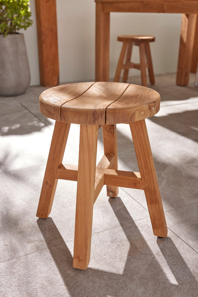 The round 'Cara' wooden outdoor stool, one of Remarkable Outdoor Living's best pieces of wooden outdoor furniture, displayed in a sunny outdoor area on stone tiling.