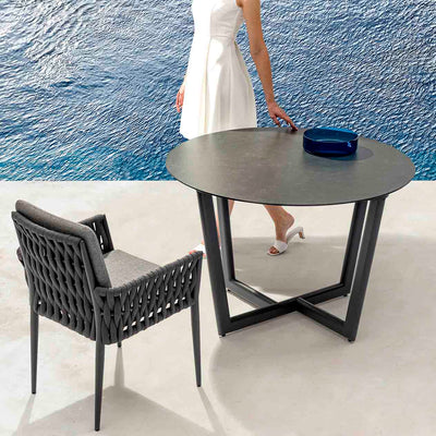 Black Colwood outdoor aluminium round dining table with ceramic glass top 110 cm accompanied by one matching outdoor chair, set poolside during summer. The alfresco furniture offers a stylish and comfortable spot for outdoor dining, perfect for enjoying warm weather by the pool.