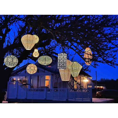 A cluster of Lumiz outdoor lanterns hanging from a tree at night, creating a warm and cozy atmosphere right outside a home, enhancing outdoor living.