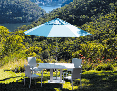 Blue outdoor umbrella covering outdoor furniture in a greenery area on a hill, overlooking Australian nature, shading a table and four chairs for a relaxing outdoor living experience.