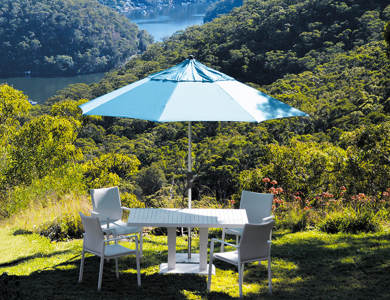 Blue outdoor umbrella covering outdoor furniture in a greenery area on a hill, overlooking Australian nature, shading a table and four chairs for a relaxing outdoor living experience.