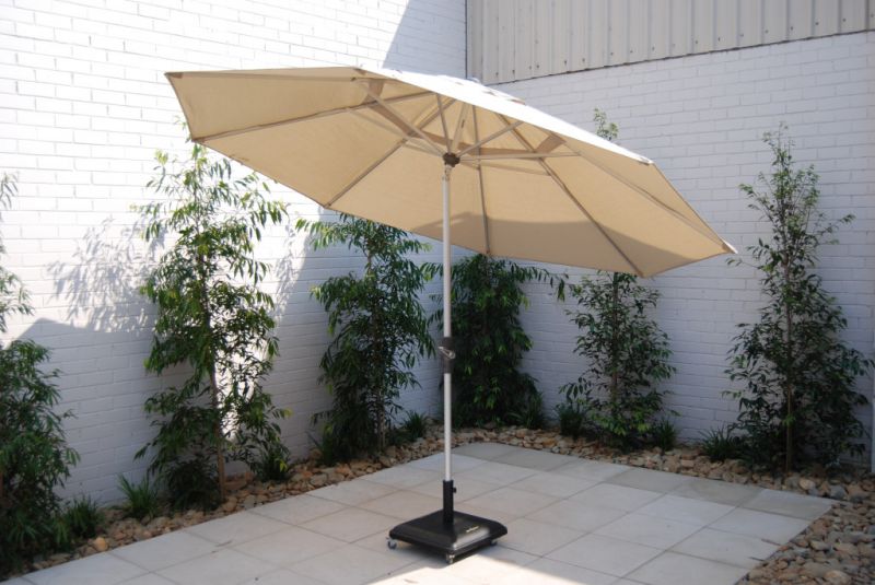 Light brown outdoor umbrella offering shade to a stone outdoor area with small trees in the background, ideal for outdoor living.