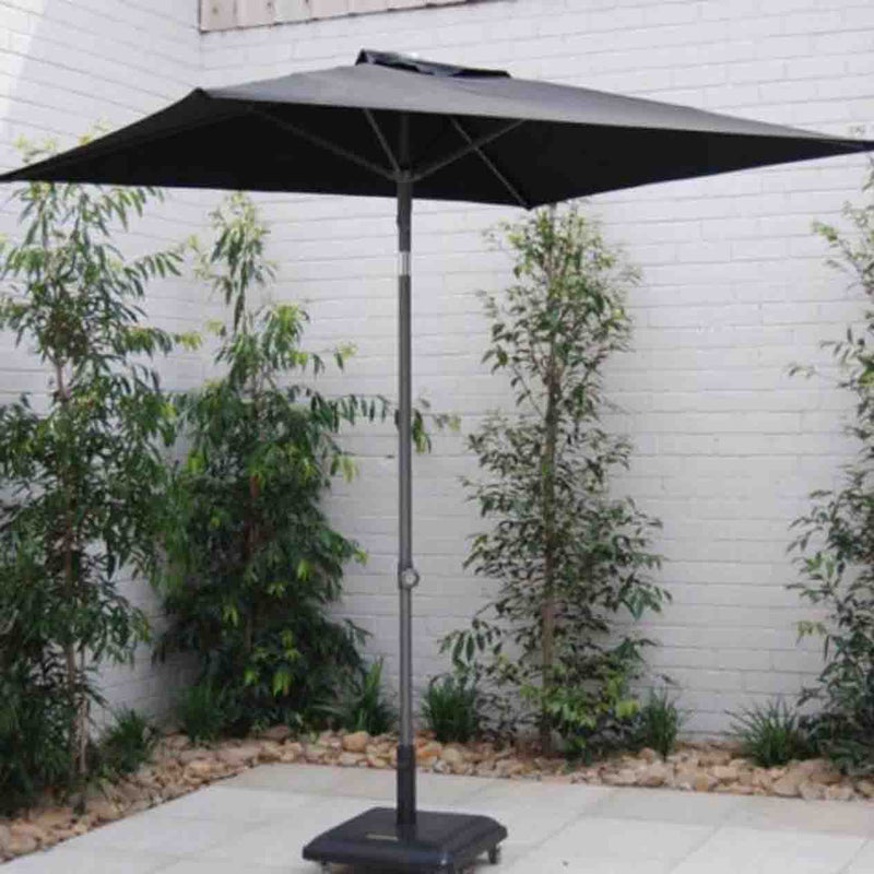 Black outdoor umbrella set in an outdoor area with a white wall and greenery in the background, providing stylish shade and UV protection.