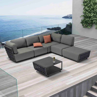 Dark-grey Lawson 5-seater outdoor rope modular lounge with two orange throw pillows, complemented by a matching Lawson outdoor coffee table with a small succulent plant, all set on a wooden deck of a modern house overlooking the ocean, creating a chic and inviting outdoor living space.