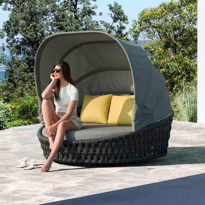Rope daybed with two yellow pillows, a woman relaxing on it under the summer sun, surrounded by lush greenery, embodying the essence of outdoor living.