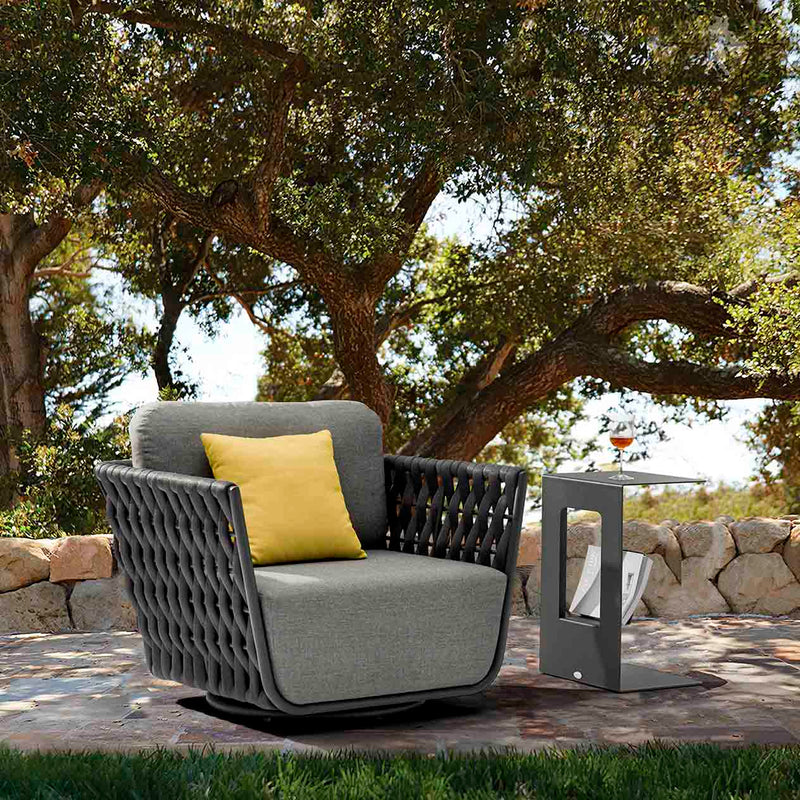 Dark grey Lawson outdoor rope swivel chair with a yellow pillow, paired with an aluminium side table holding a drink, set in a sunny outdoor area with a tree in the backgroundan inviting setup for relaxed outdoor living during summer.