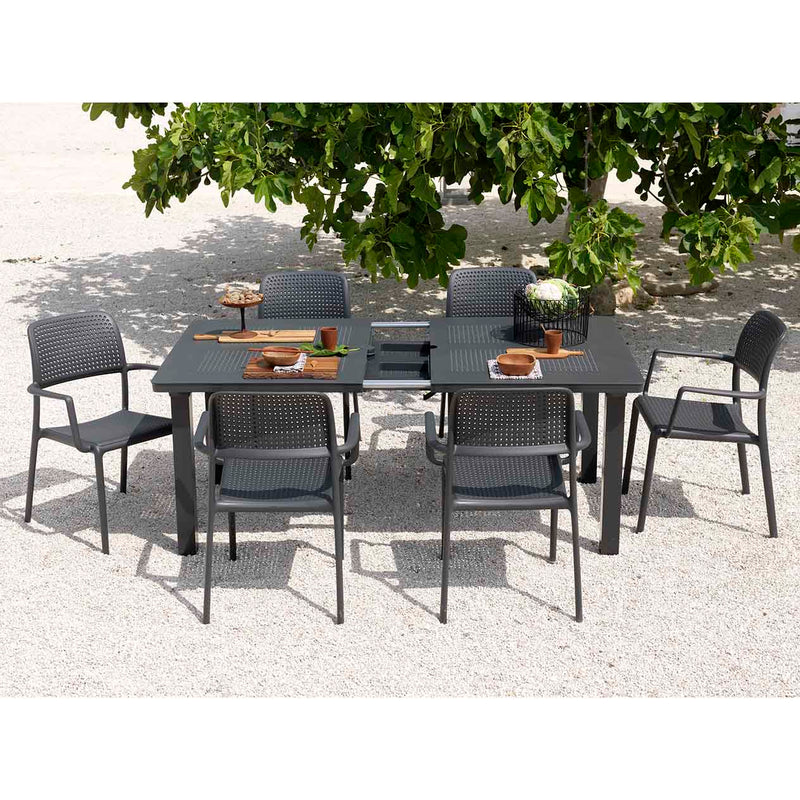 Black resin extension dining table with six matching chairs, set in an outdoor area as alfresco furniture, with the table styled with wooden cutlery for a refined look.