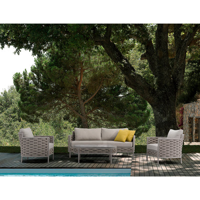 Boston Outdoor Rope Coffee Table with two wine glasses and a rolled-up magazine, surrounded by two Boston Outdoor Rope Armchairs and a Boston 2-Seater Outdoor Rope Lounge, all in beige, set poolside on a wooden deck with trees in the background, showcasing luxurious alfresco furniture.