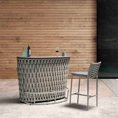A single beige Boston Outdoor Rope Bar Stool paired with a small bar table holding glasses and drinks, set against a wooden deck wall backdrop, embodying elegant outdoor living.