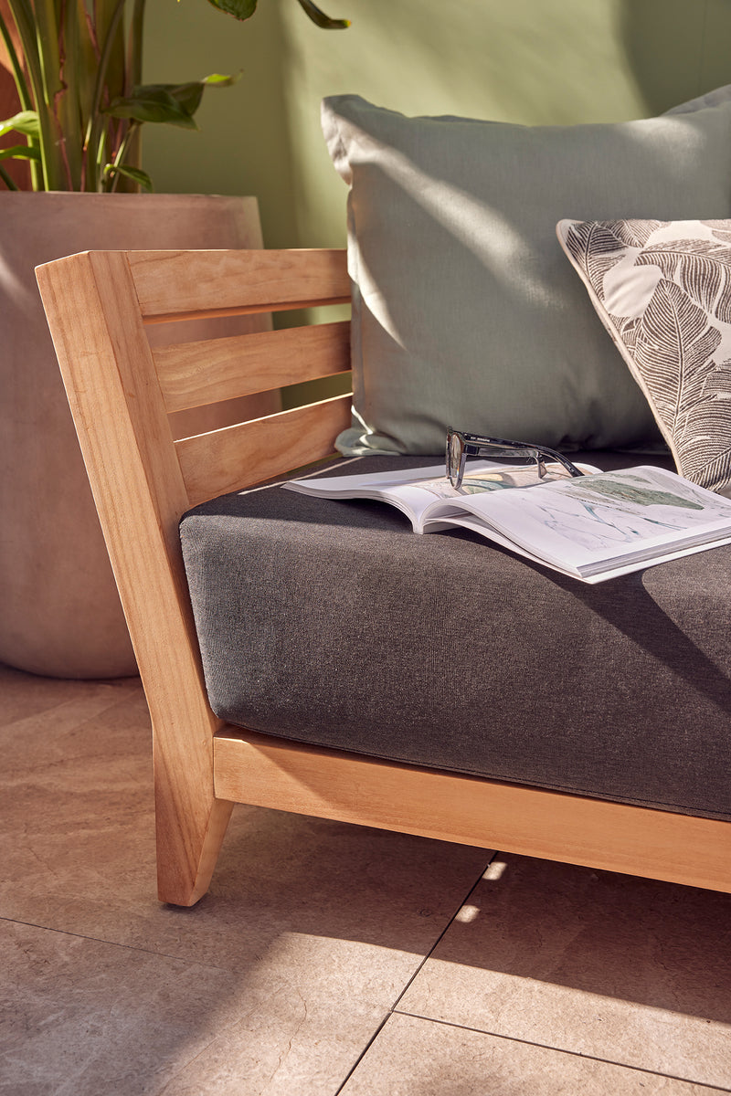 Outdoor balcony furniture set from The Ottawa family, featuring outdoor chairs, outdoor lounge, and daybed, all made of durable teak wood and Sunproof fabric, with a couch holding a book and glasses.