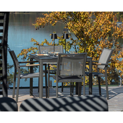 Four Largo Outdoor Aluminum Dining Chairs surrounding a small dining table on a wooden deck outdoors, overlooking serene water, showcasing stylish aluminium patio chairs for outdoor living.