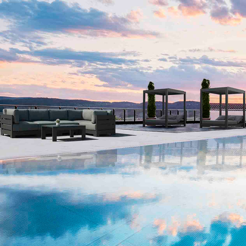 Two Skyline daybeds in the background by the pool, with a lounge and coffee table in the foreground, set against a breathtaking orange-hued sky during sunrise or sunset, ideal for serene outdoor living.