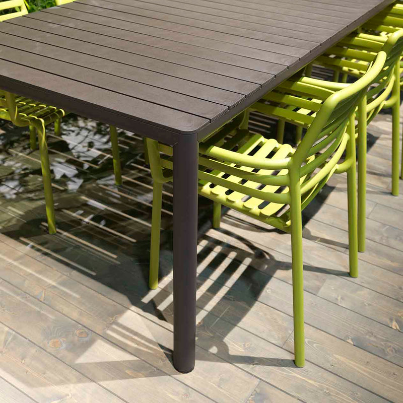 Brown Nardi Tevere outdoor extension dining table with 5 green chairs on a wooden deck, sun shining down for a perfect alfresco furniture arrangement.