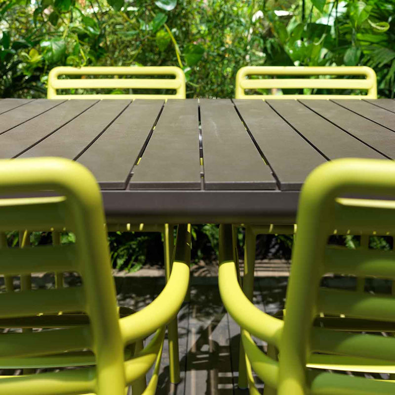 Close-up of brown Nardi Tevere outdoor extension dining table with 4 green chairs, surrounded by lush greenery, creating a perfect alfresco furniture setting.