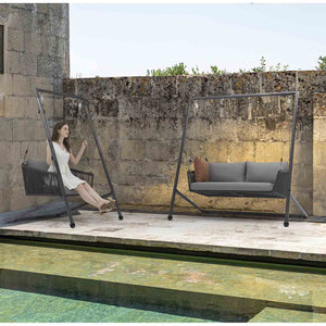 Two Truro Outdoor Rope Hanging Chairs set poolside in a European house outdoor area with stone walls, one chair occupied by a woman swinging and enjoying the moment, creating a vibrant outdoor living space.
