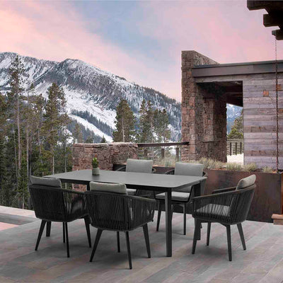 Black Truro outdoor aluminum dining table with a ceramic glass top, accompanied by five matching outdoor rope chairs, set on a wooden deck with snowy European mountains in the background during a picturesque pink-hued sunsetperfect for refined outdoor living.