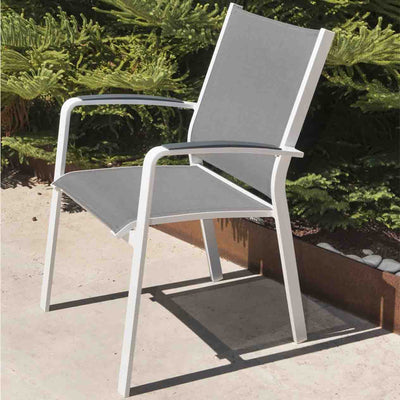 A sleek white and grey Cosmo outdoor dining chair made from durable aluminium, set in a sunlit outdoor area with lush greenery in the background, perfect for outdoor dining and relaxation with aluminium patio chairs.