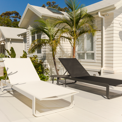 One black and one white aluminium and textilene 'Verona' sun lounger positioned in a sunny outdoor area of someone's house, with the sun beaming down on the loungers.