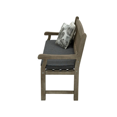 A 150cm dark brown wooden outdoor bench with a dark grey fade-resistant seat cushion & 2 light-coloured decorative throw pillows. The bench is made of high-quality acacia wood, and perfect for any outdoor setting. It is displayed on a plain white background, viewed from the side.