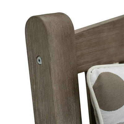 A close-up on the backrest of a 150cm dark brown wooden outdoor bench with a light-coloured decorative throw pillow. The bench is made of high-quality acacia wood, and perfect for any outdoor setting. It is displayed on a plain white background.