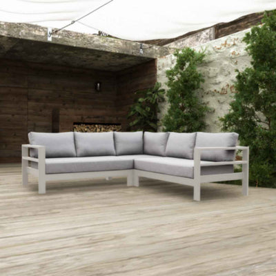 An aluminium 5-seater Modular Lounge with white frame and light grey fabric set outdoors with greens and a woodpile in the background. Outdoor furniture, outdoor lounge chair, aluminium outdoor furniture.