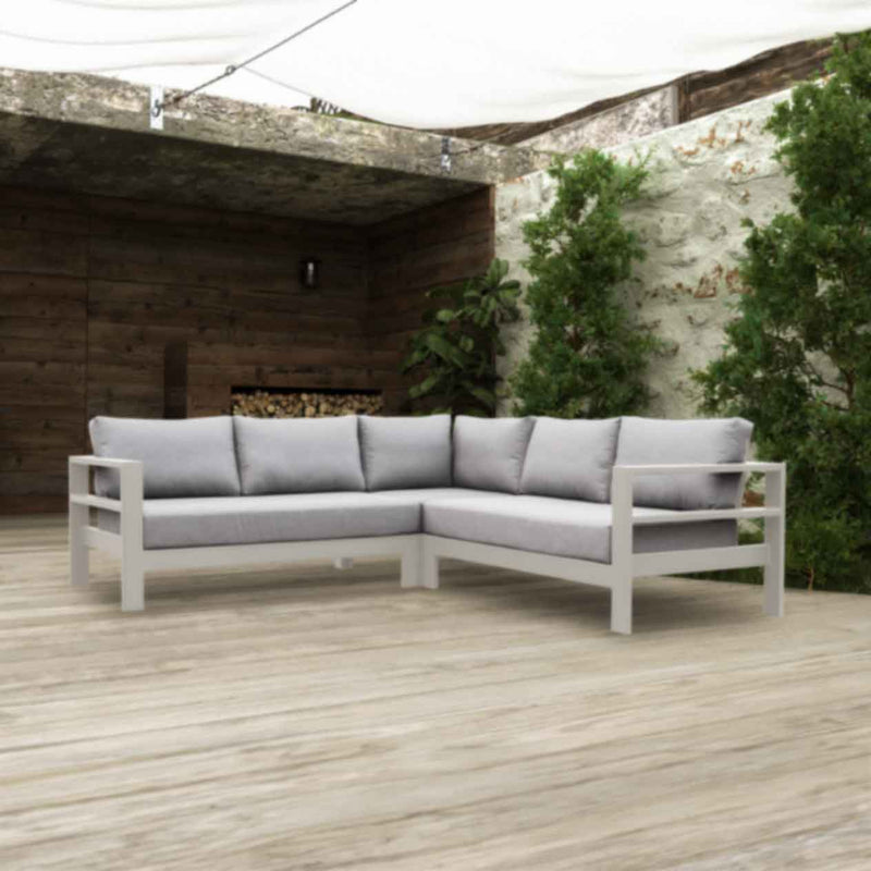An aluminium 5-seater Modular Lounge with white frame and light grey fabric set outdoors with greens and a woodpile in the background. Outdoor furniture, outdoor lounge chair, aluminium outdoor furniture.